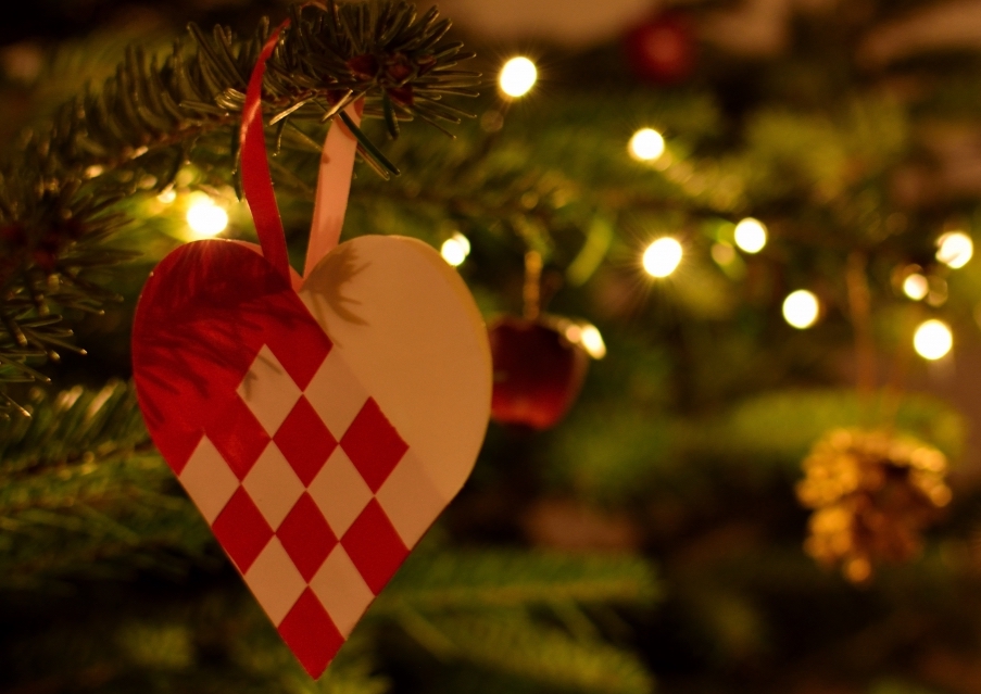 A red and white woven paper heart ornament hangs on a Christmas tree